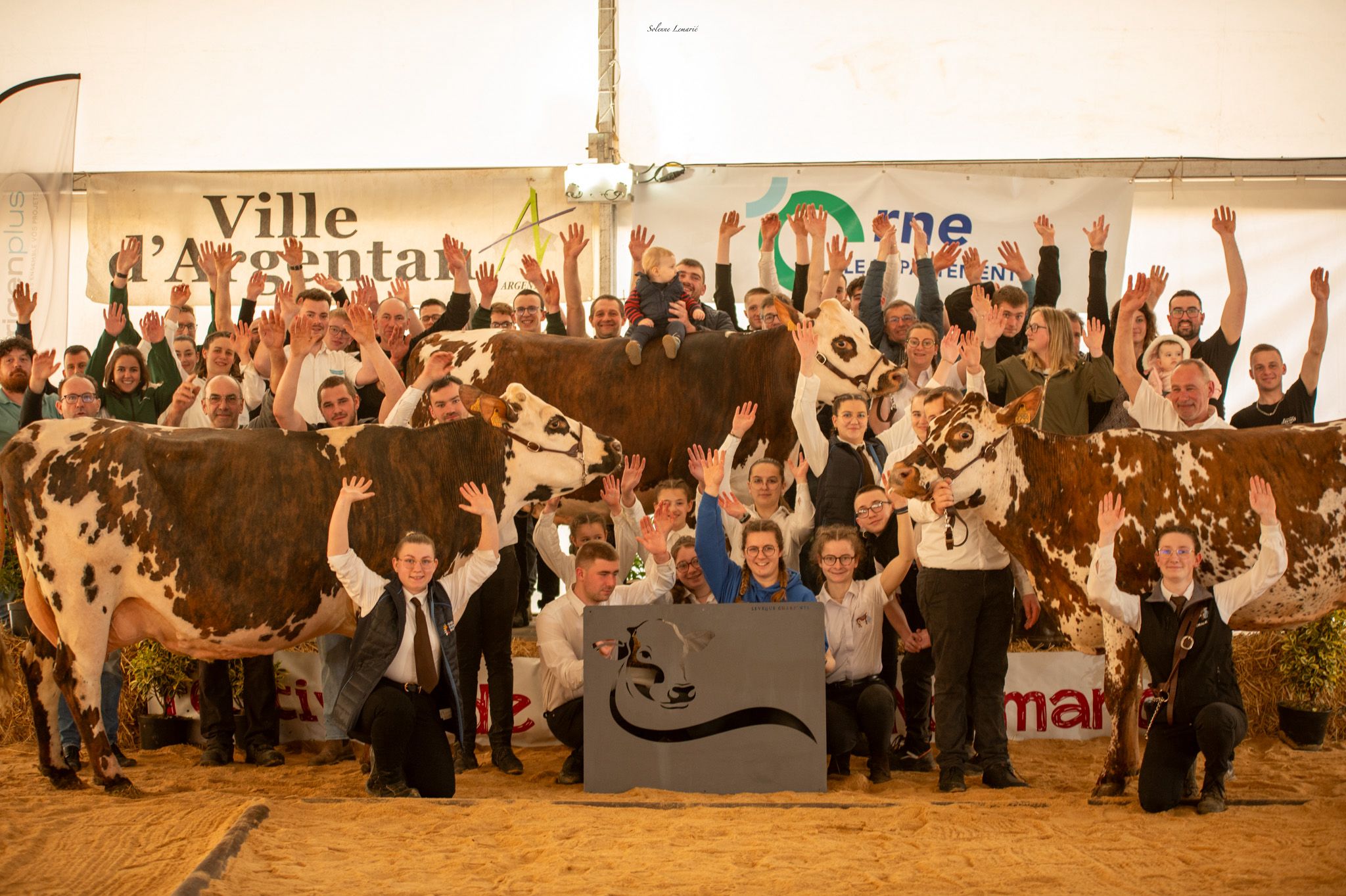 Groupe d’éleveurs et d’éleveuses posant sur un ring avec plusieurs vaches de race Normande lors du concours départemental à la Fête de la Normandie à Argentan.